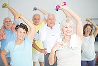 Auf dem Bild sind drei Frauen und drei Männer im Seniorenalter in einem Sportraum. Sie machen gemeinsam eine Gymnastikübung, bei der sie die Hände über den Kopf heben.