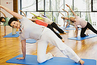 Auf dem Bild sind mehrere Frauen zu sehen, die sportlich gekleidet sind. Sie machen gemeinsam Yogaübungen auf Yogamatten.