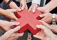 Auf dem Bild sind mehrere Hände zu sehen, die das rote Kreuz aus Kunststoff an den Ecken halten. Die Hände formen zusammen einen Kreis um das Kreuz.